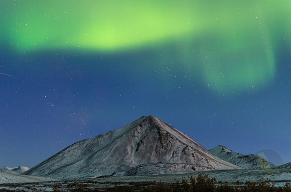 The northern lights hover over a lonely mountain in the Brooks Range of Alaska.