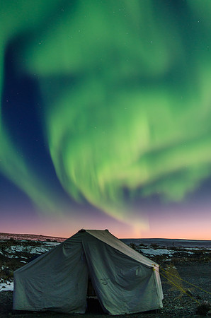 The northern lights dance over the cook tent while the Alaskan summer sun hangs just below the horizon.