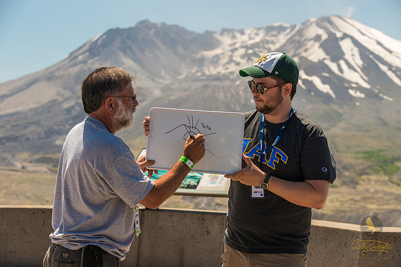 Dr. Jim Beget, with Mount St. Helens in the background, draws for the students a diagram depicting the events of the famous 1980 eruption. GeoFORCE counselor, Patrick Graham plays assistant.